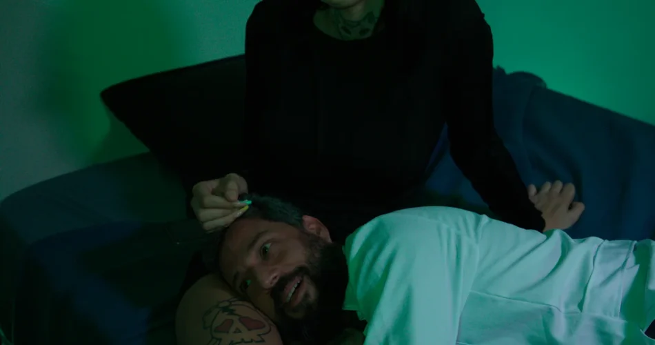 Mulher rindo com um homem deitado no colo, sob luz verde