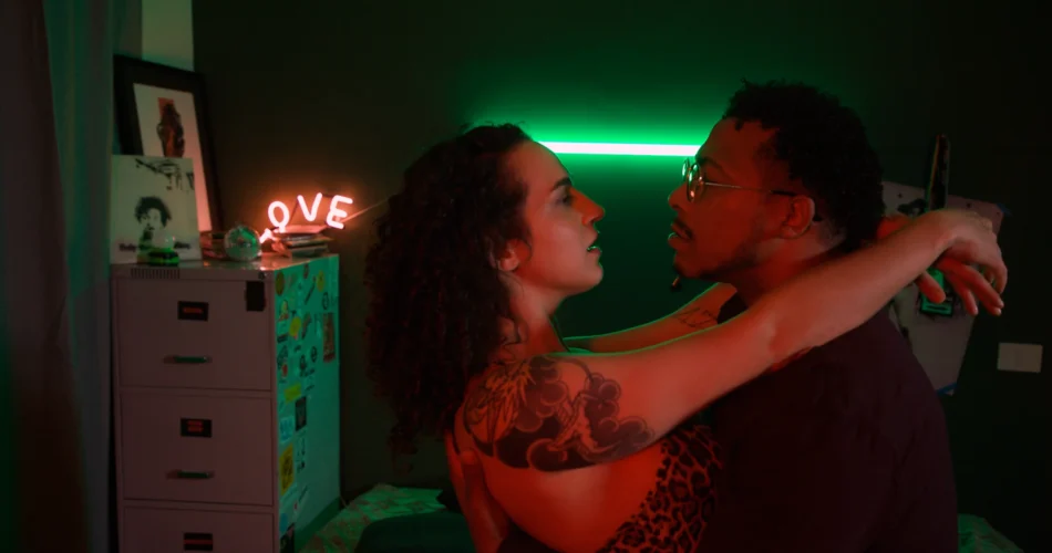 Casal abraçado sob neon verde e letreiro LOVE