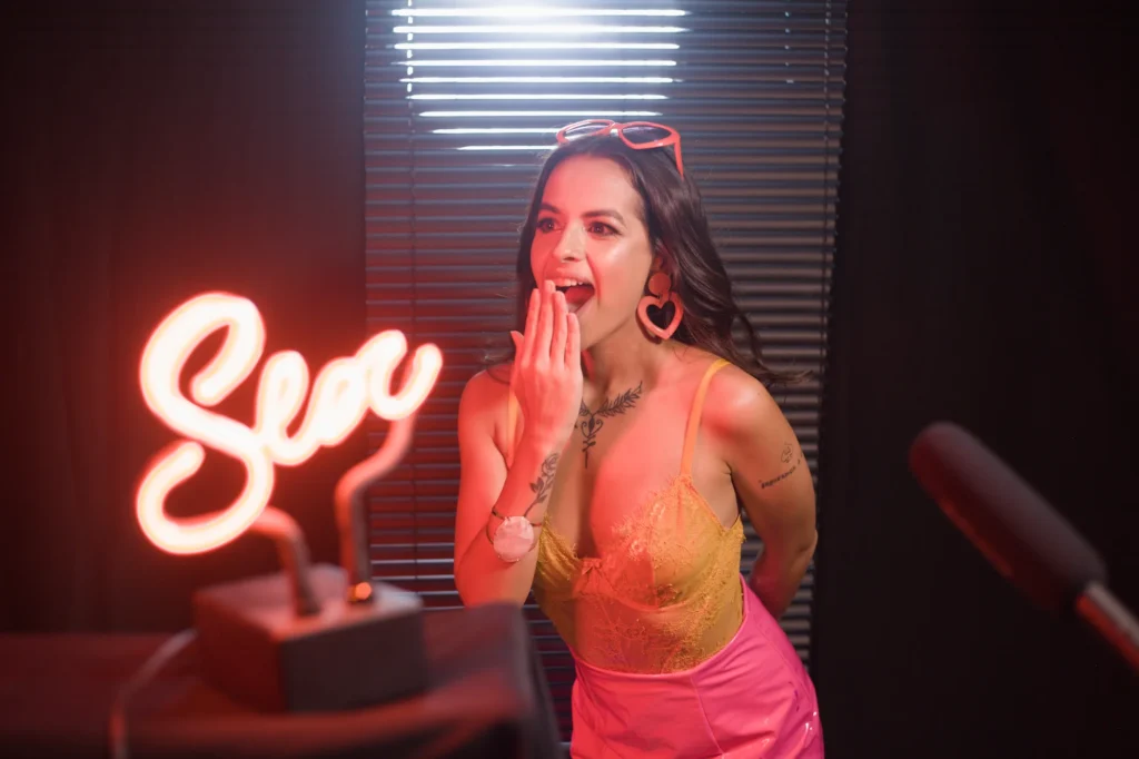 Mulher de body rendado ao lado de um letreiro neon