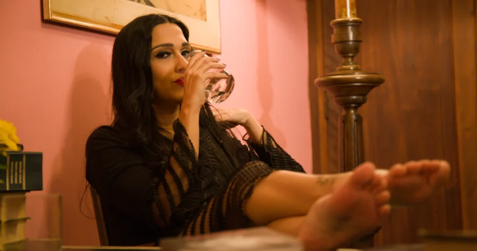 Mulher bebendo com os pés descalços apoiados na mesa